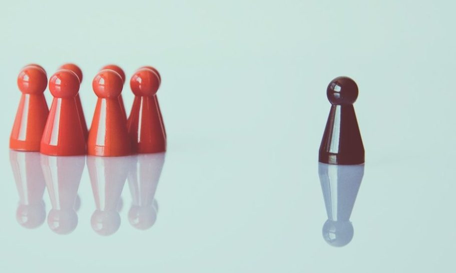 Fünf rote Spielfiguren stehen links, eine schwarze Figur steht allein rechts als Symbol für den einen perfekten Mitarbeiter.
